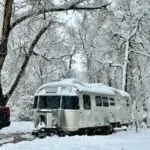 Snow falls all around Ellie the Airstream, amid a forest heavy with wet snow.