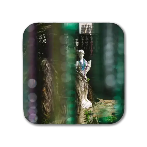 A coaster featuring a New Orleans picture of a classic Greek sculpture of a woman wearing Mardi Gras beads