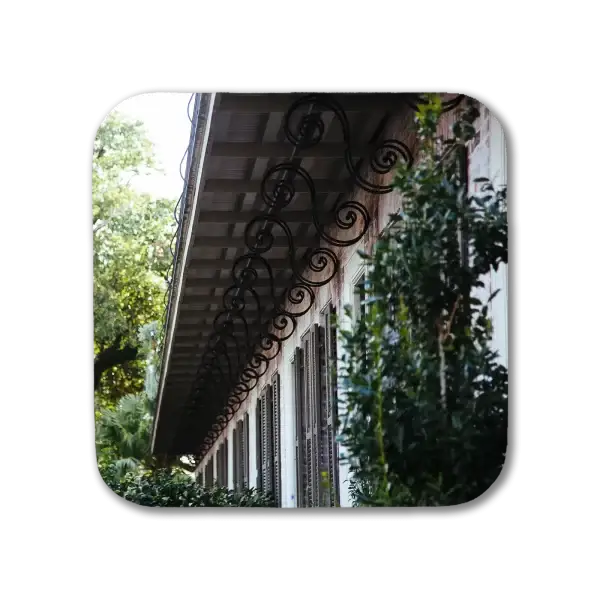 A coaster featuring a New Orleans picture of decorative wrought iron underlying a long building's balcony