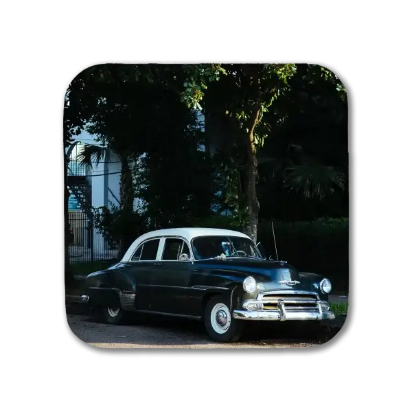 A coaster featuring a New Orleans picture of a classic car with two-tone paint parked in front of a large magnolia tree