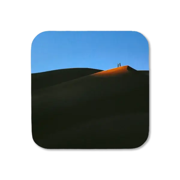Two people stand atop a dune with their surroundings in shade at sunset, except for a small patch of sand around where they're standing, artwork for a coaster
