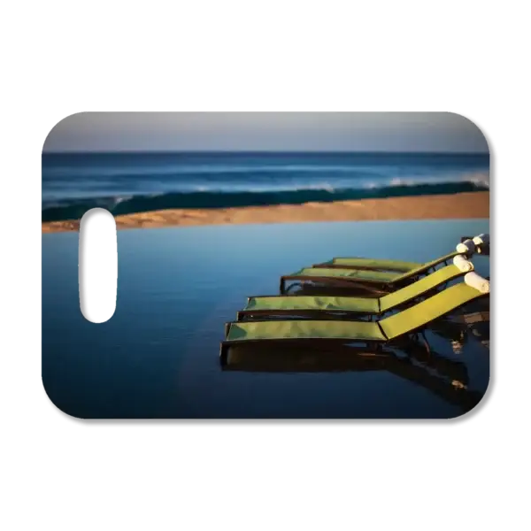 Premium luggage tag featuring a Mexican resort with lounge chairs at the edge of an infinity pool with the beach and ocean in the background.