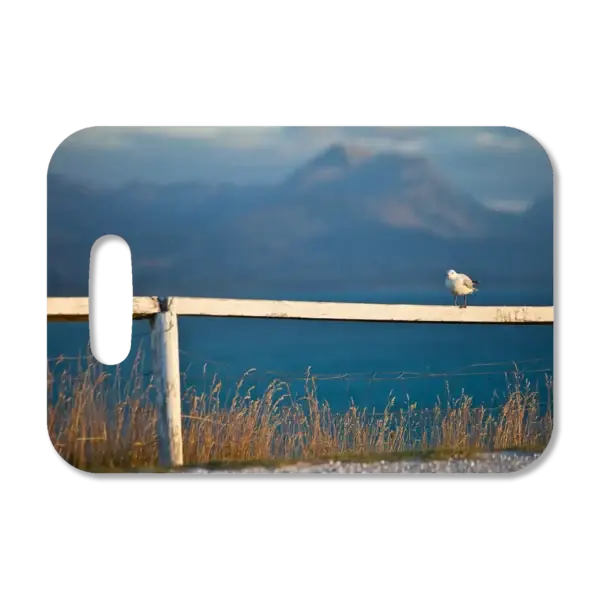 Premium luggage tag featuring a New Zealand seagull standing along a fence with the ocean in the background.